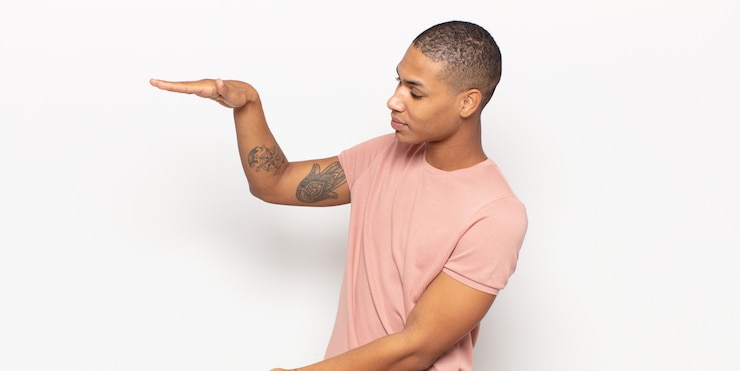 Foto jovem negro segurando um objeto com as duas mãos no espaço lateral de cópia, mostrando, oferecendo ou anunciando um objeto