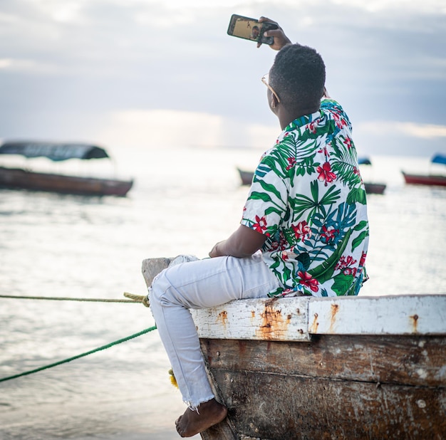 Jovem negro sentado em um barco fazendo uma selfie sozinho