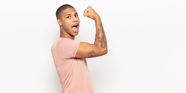 jovem negro sentindo-se feliz, satisfeito e poderoso, flexionando a forma e bíceps musculosos, parecendo forte depois da academia
