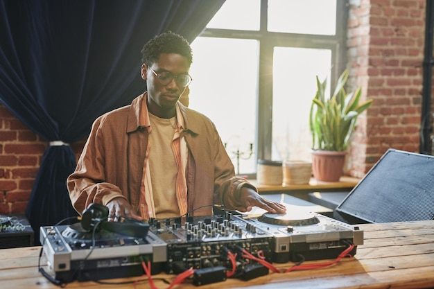 Jovem negro sério olhando para dj board enquanto toca toca-discos