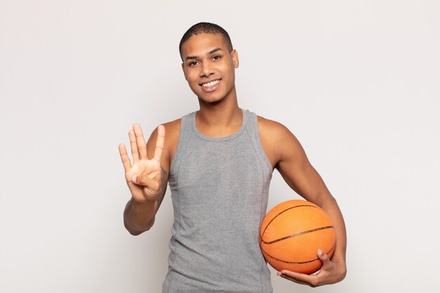 jovem negro sorrindo e parecendo amigável, mostrando o número quatro ou o quarto com a mão para a frente, em contagem regressiva