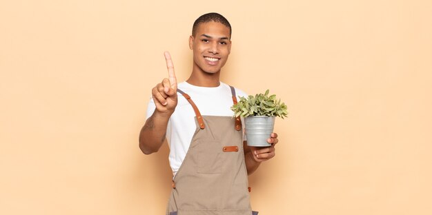 Jovem negro sorrindo e parecendo amigável, mostrando o número um ou o primeiro com a mão para a frente, em contagem regressiva