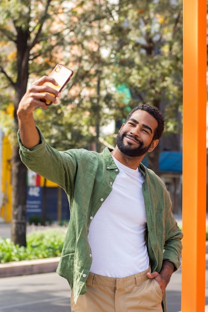 Jovem negro sorrindo tirando uma selfie na rua