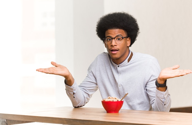 Jovem negro tomando café da manhã confuso e em dúvida