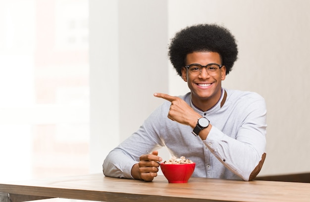 Jovem negro tomando café da manhã sorrindo e apontando para o lado