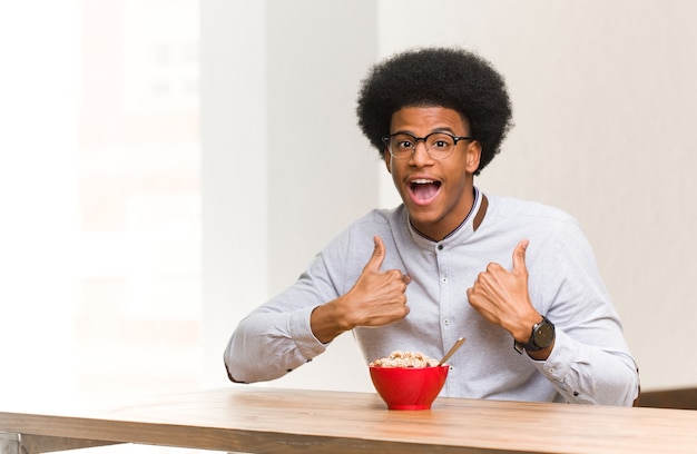 Jovem negro tomando café da manhã surpreso, se sente bem-sucedido e próspero