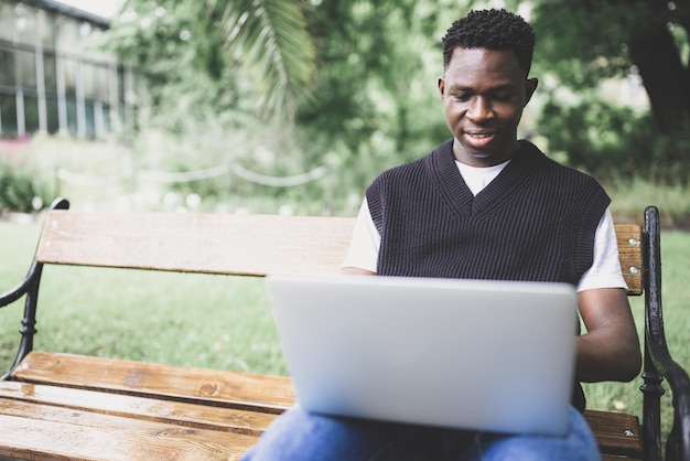 Jovem negro trabalhando no laptop ao ar livre olhando para a tela sorrindo