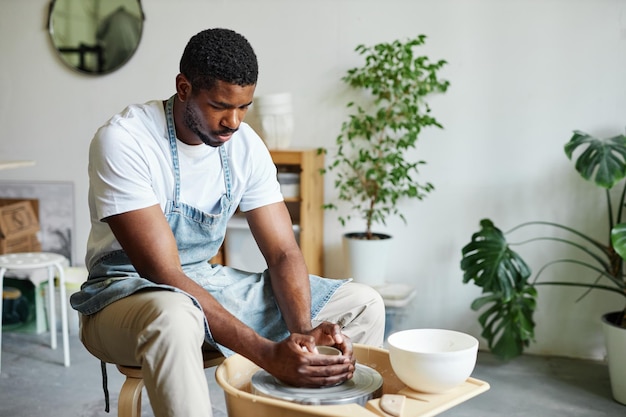 Jovem negro usando roda de oleiro e criando cerâmica artesanal