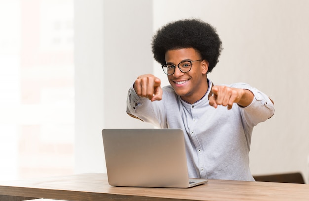 Jovem negro usando seu laptop alegre e sorridente apontando para a frente