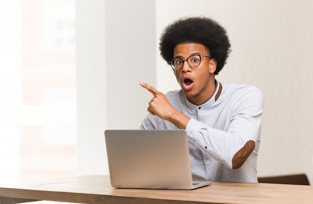 Jovem negro usando seu laptop apontando para o lado