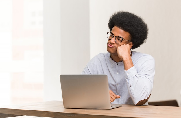 Jovem negro usando seu laptop, pensando em algo, olhando para o lado