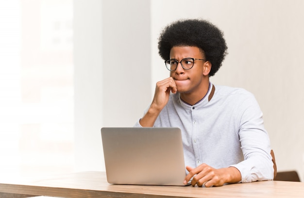 Jovem negro usando seu laptop, pensando em uma idéia