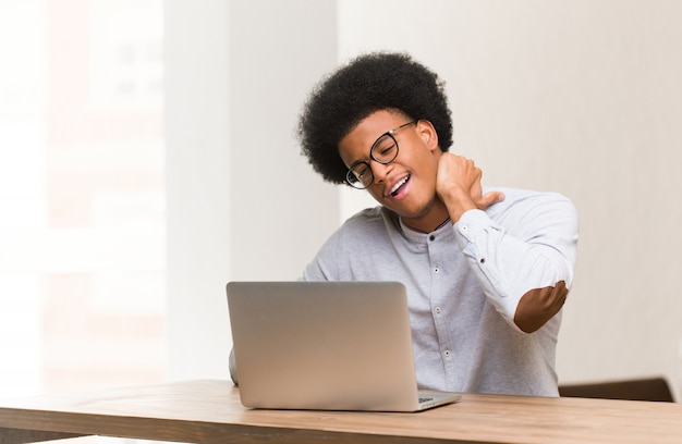 Jovem negro usando seu laptop, sofrendo de dor no pescoço