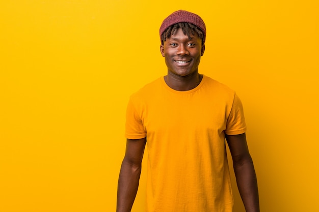 Jovem negro vestindo rastas sobre parede amarela feliz, sorridente e alegre.