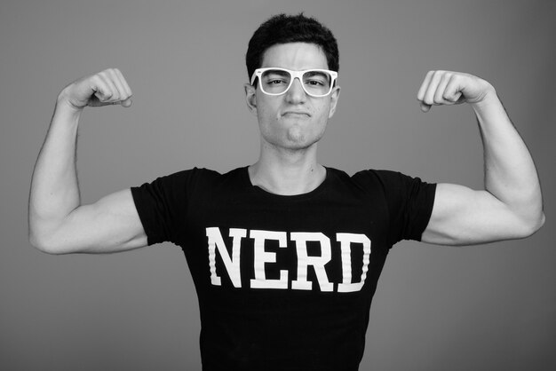 Foto jovem nerd bonito com óculos contra uma parede cinza