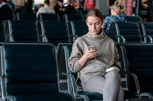 Jovem no aeroporto esperando sua partida. Smartphone de rolagem.