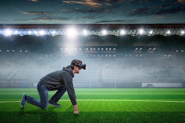 Jovem no fone de ouvido VR na posição pronta para começar em um estádio. Mídia mista