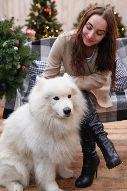 Jovem no fundo da árvore de Natal com cachorro samoiedo branco ao ar livre Decoração de quintal para o Ano Novo