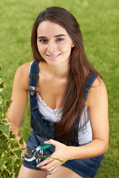 Foto jovem no jardim aparando folhas e jardinagem natureza e sorriso em retrato com primavera e flores plantação de botânica e jardineira feminina é paisagismo ao ar livre no quintal e juventude feliz