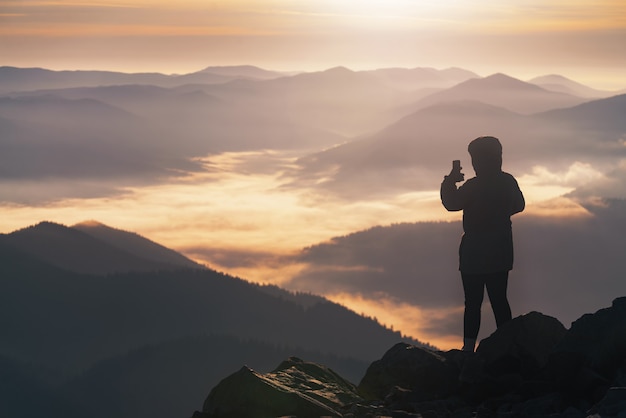 Jovem no pico da montanha fotografa ao telefone uma bela paisagem montanhosa ao nascer do sol.