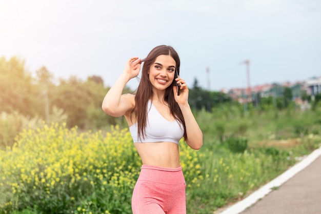 Jovem no sportswear falando no telefone ao ar livre enquanto faz uma pausa entre o treinamento,