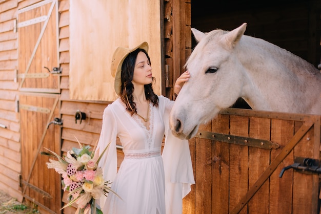 Jovem noiva em estilo boho acariciando o cavalo branco