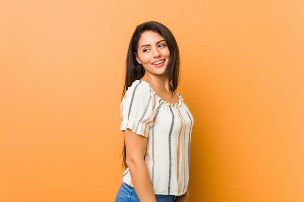 Jovem olha de lado sorrindo, alegre e agradável.