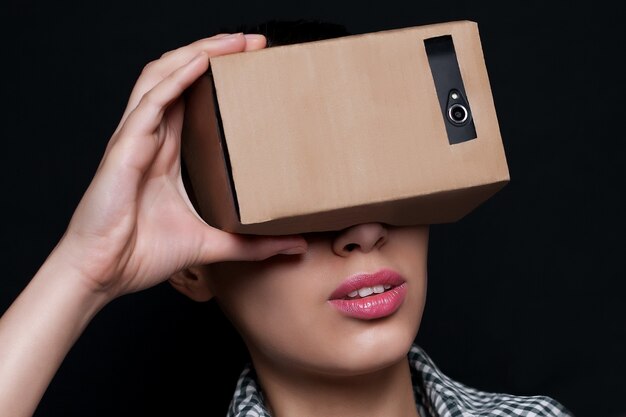 Foto jovem olhando através de um fone de ouvido de papelão de realidade virtual