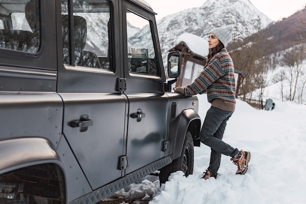 Jovem olhando para a montanha de neve encostada em seu carro nos alpes italianos.