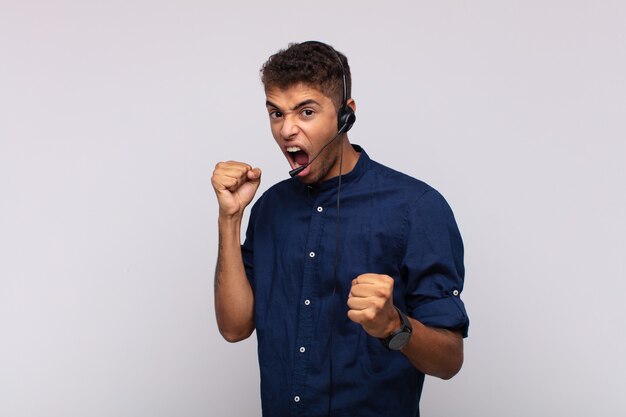 Foto jovem operador de telemarketing gritando agressivamente com uma expressão de raiva ou com os punhos cerrados celebrando o sucesso