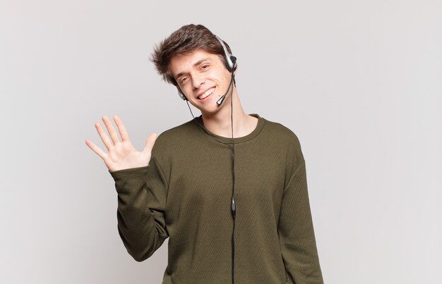 Jovem operador de telemarketing sorrindo e parecendo amigável, mostrando o número cinco ou quinto com a mão para a frente, em contagem regressiva