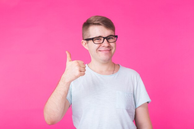 Jovem otimista em fundo rosa mostrando os polegares com emoções positivas