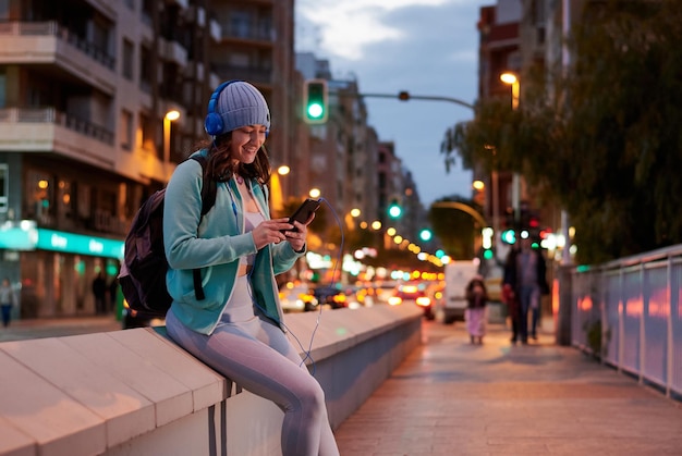 Jovem ouve música em fones de ouvido com luzes da cidade ao entardecer