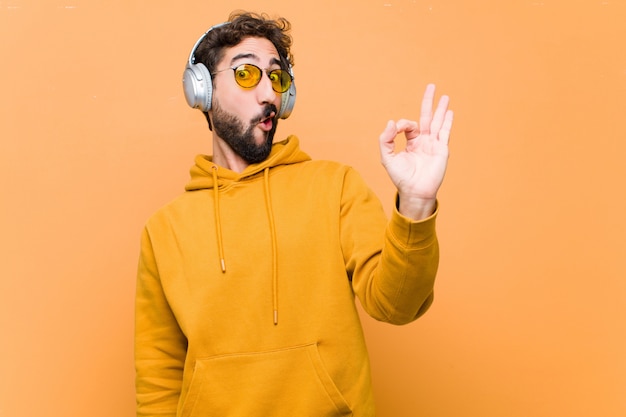 Jovem ouvindo música com fones de ouvido contra parede laranja