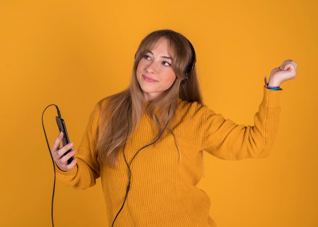Jovem, ouvindo música no seu smartphone feliz com fones de ouvido no fundo amarelo