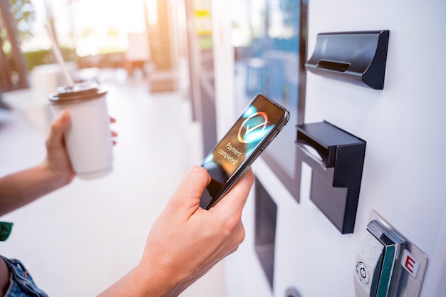 Jovem pagando café em uma máquina de venda automática usando método de pagamento sem contato