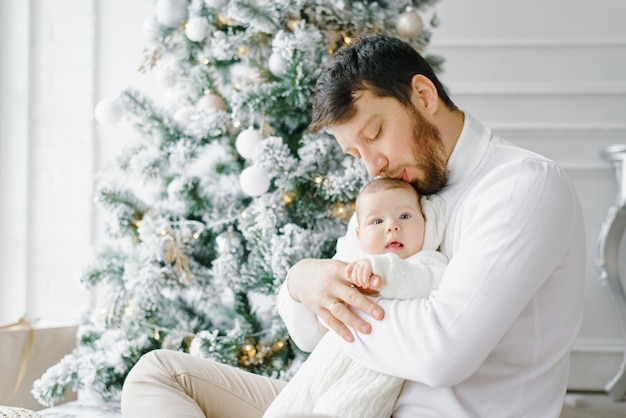 Jovem pai beija o filho pequeno e senta-se perto da árvore de Natal