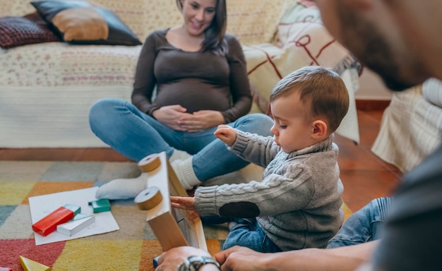 Jovem pai brincando com seu filho um jogo de madeira na sala de estar enquanto a mãe está olhando para eles