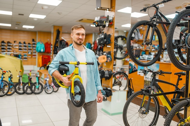 Jovem pai com bicicleta infantil, fazer compras na loja de esportes.