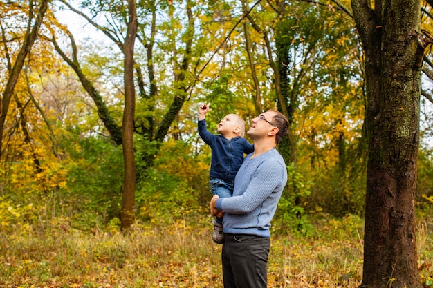 Jovem pai com um filho pequeno segurando olhando para a castanha, caminhando e estudando a natureza