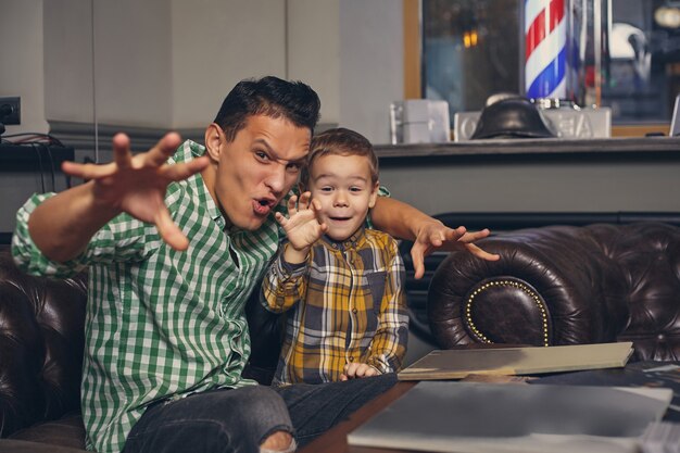 Jovem pai e seu filho estiloso na barbearia na sala de espera