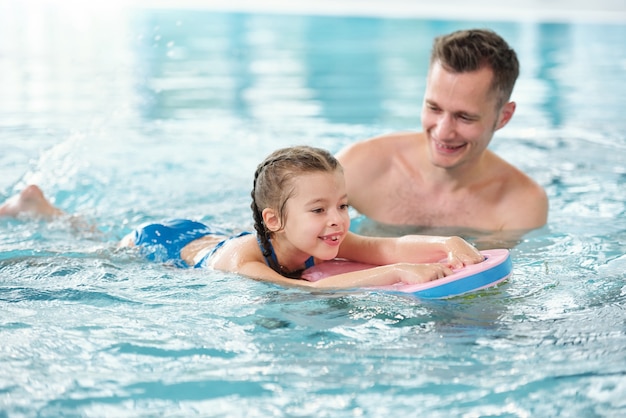 Jovem pai feliz ensinando sua adorável filha a nadar na piscina enquanto passa o tempo ou as férias em um spa ou resort de verão