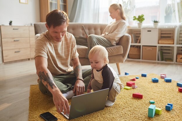 Jovem pai sentado no chão assistindo desenhos no laptop junto com o filho e a mãe