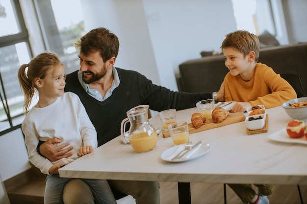 Jovem pai tomando café da manhã com seu filho e filha em casa