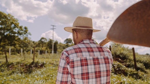 Jovem para trás na camisa casual segurando sua enxada na fazenda Ferramenta agrícola Homem latino