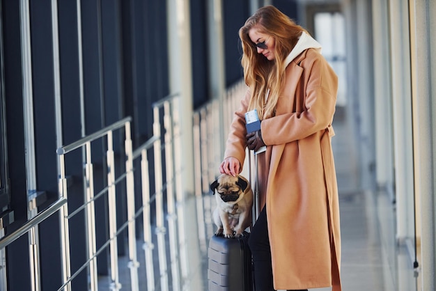 Jovem passageira em roupas quentes andando com seu cachorro no saguão do aeroporto.