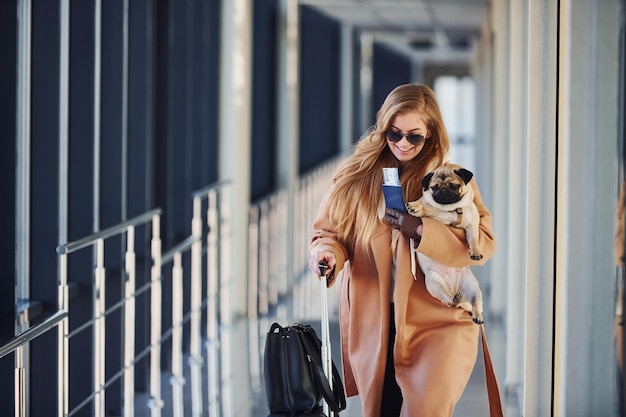 Jovem passageira em roupas quentes andando com seu cachorro no saguão do aeroporto.