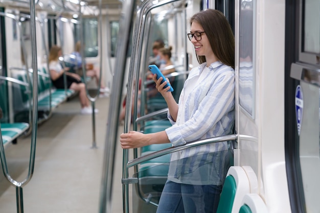 Jovem passageira usando telefone celular inteligente, conversando em redes sociais no trem do metrô