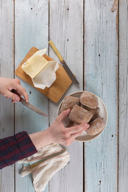 Jovem passando manteiga em um pão em uma velha mesa rústica.
