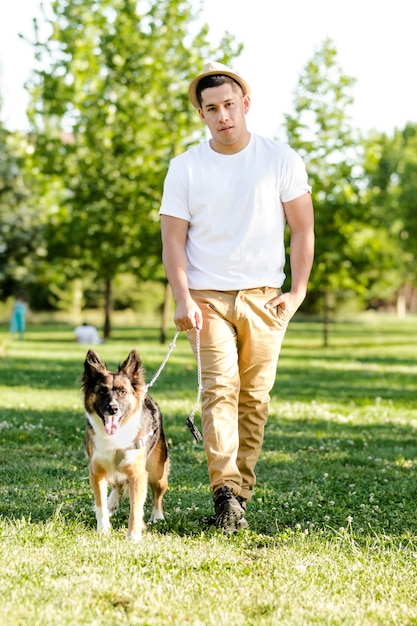 Jovem passeando com o cachorro no parque. modelo latino posando e assistindo na câmera